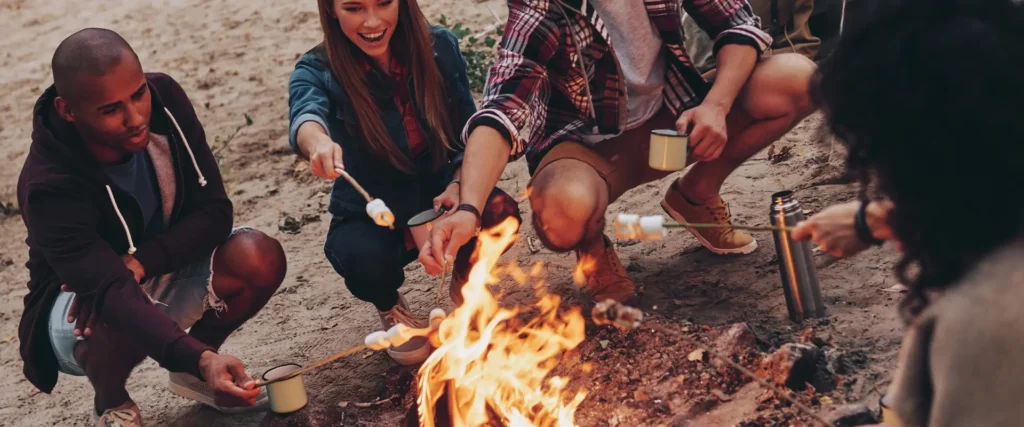 Employees enjoying a bonfire and roasting marshmallows during a team trip, representing affordable and meaningful recognition experiences.